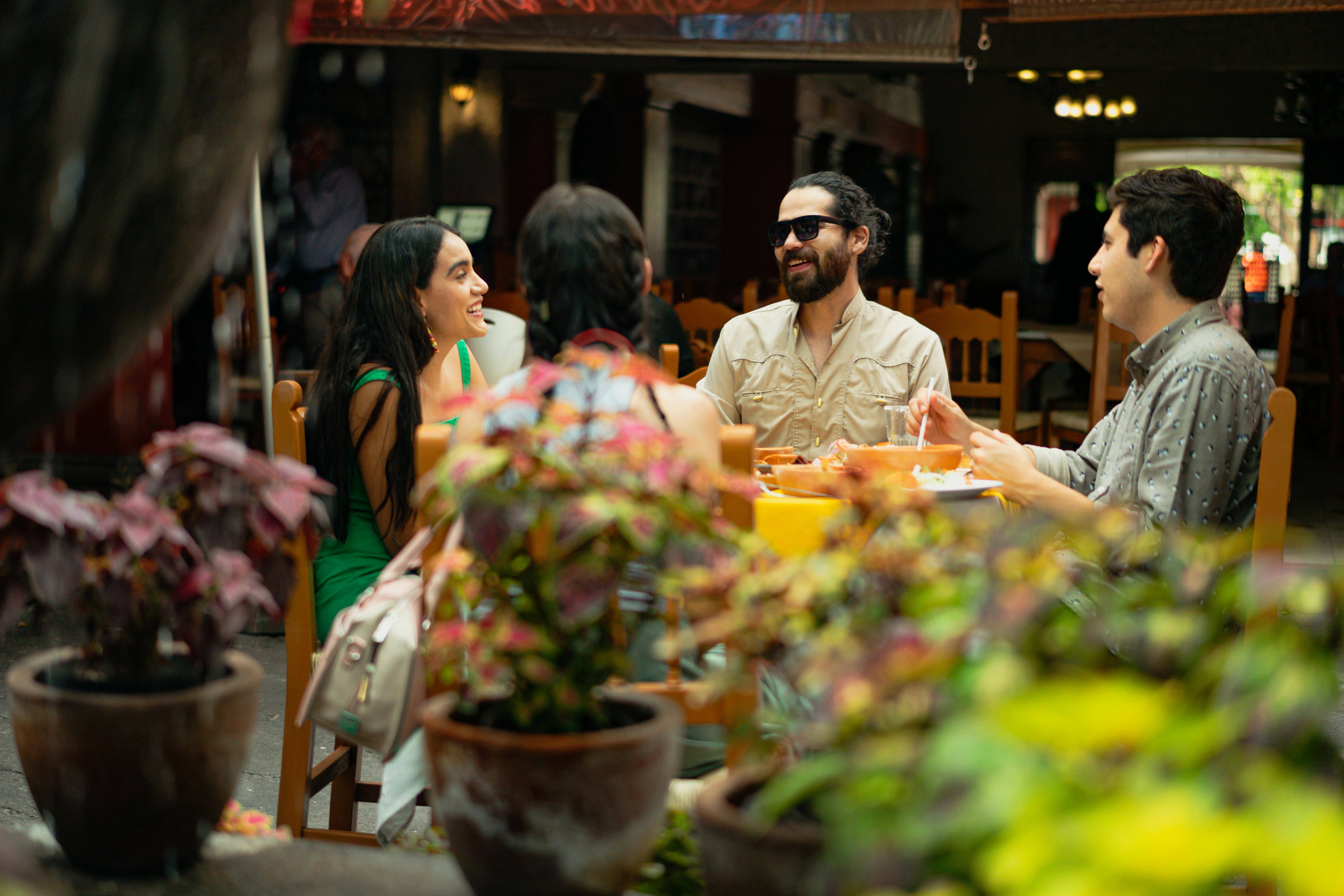 Lachende Gäste sitzen an einem Tisch im Außenbereich eines Restaurants und unterhalten sich